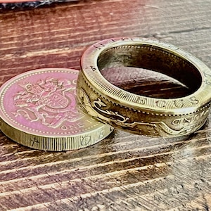 May include: A gold-colored ring made from a British one pound coin. The ring is made from the outer rim of the coin, and the inner part of the coin is visible in the background.