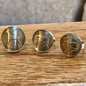 May include: Three silver coin rings, each with a different animal design: a greyhound, a bull, and a rabbit. The rings are displayed on a wooden surface.