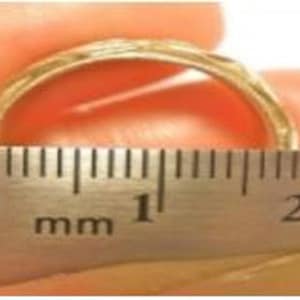 May include: A gold-colored ring with a textured design is held next to a ruler. The ruler shows measurements in millimeters. The ring's width is approximately 10 mm.