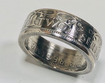 Puede incluir: Un anillo de plata con texto grabado y elementos decorativos. El anillo parece estar hecho de una moneda, con las palabras "TWO SHILLINGS" y "ATIA REGINA". El borde del anillo tiene una textura.