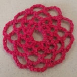 Pode incluir: Uma flor de crochê rosa com formato circular e várias camadas.