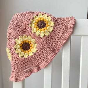 Blush pink crochet bucket hat with sunflowers around the middle of the hat.
