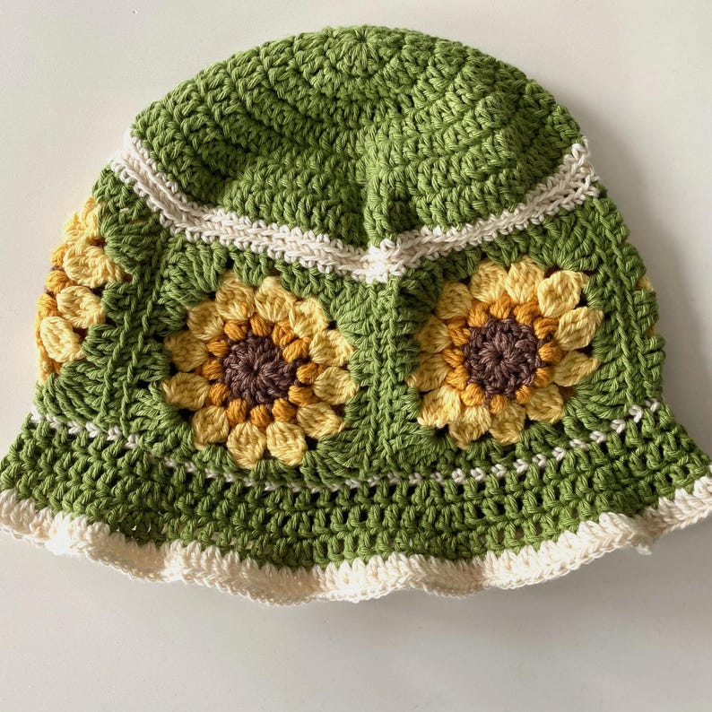 Clos up of green crochet sunflower bucket hat with cream edging and sunflowers around the middle of the hat.
