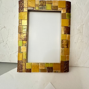 Puede incluir: Un marco de fotos de mosaico dorado y marrón con fondo blanco. El marco está hecho de pequeñas baldosas cuadradas.