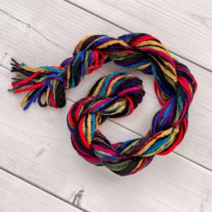 May include: A multi-colored braided cord with a fringe on one end. The cord is made of velvet and is twisted together in a rope-like pattern. The colors are red, blue, green, yellow, and black.
