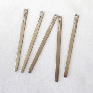 May include: Five silver metal threader tools, each with a small hole in the center, are arranged in a fan shape on a white surface.