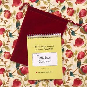 May include: A yellow booklet with a spiral binding titled "my Little Loom Companion" by Lucy Jennings. The booklet has the text "All the basic weaves at your fingertips!" and "Slow down and make it with love." The booklet is sitting on a red velvet bag.