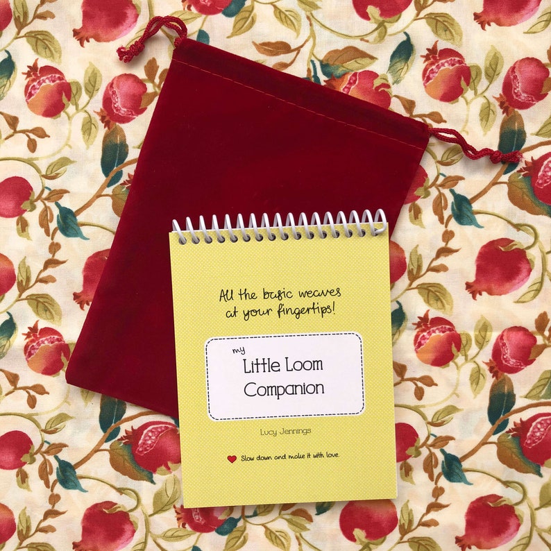 May include: A yellow booklet with a spiral binding titled "my Little Loom Companion" by Lucy Jennings. The booklet has the text "All the basic weaves at your fingertips!" and "Slow down and make it with love." The booklet is sitting on a red velvet bag.