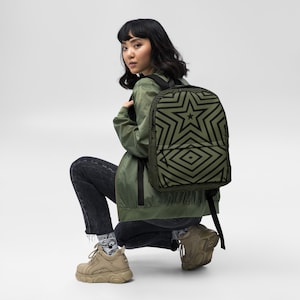 May include: A person wearing a green jacket and black jeans is wearing a black and green backpack with a geometric star pattern.
