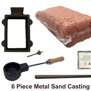 May include: A 6-piece metal sand casting kit. The kit includes a black metal mold, a package of sand, a crucible with a wooden handle, a stirring rod, a small brass tool, and a packet of borax powder. The text "BLACK BARN DESIGN" is visible.