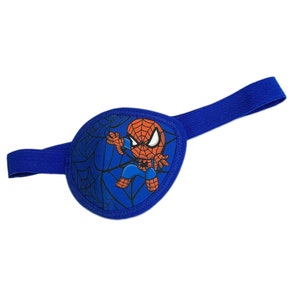 Può includere: Parche per l'occhio blu con un cinturino elastico. Il cerotto presenta un'immagine di cartone animato di Spiderman con un costume rosso e blu, che si dondola su una ragnatela.
