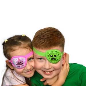 Pode incluir: Duas crianças, uma menina e um menino, estão usando tapa-olhos. O tapa-olho da menina é rosa com um desenho de unicórnio. O tapa-olho do menino é verde com um desenho de personagem do Minecraft. Eles estão sorrindo e se abraçando.