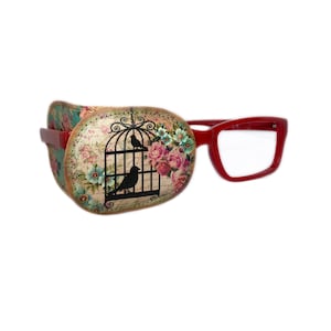 May include: A red eye patch with a floral design featuring a birdcage and birds. The eye patch is attached to a pair of red plastic glasses.