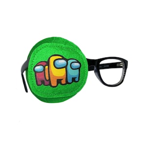 Pode incluir: Um tapa-olho verde com uma imagem impressa de quatro personagens de Among Us. O tapa-olho está preso a um par de óculos com armação preta.