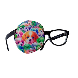 May include: A black eye patch with a colorful pattern of puppies on it. The eye patch is attached to a pair of black eyeglasses.