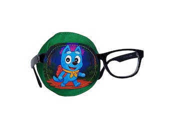 May include: A green eye patch with a cartoon dog illustration, attached to a pair of black-framed eyeglasses. The dog is blue with a red backpack and yellow scarf. The glasses have a rectangular shape.