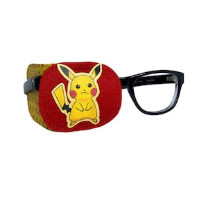 Può includere: Un paraluce per occhi in feltro rosso con un personaggio di Pikachu giallo stampato su di esso. Il paraluce è attaccato a un paio di occhiali con montatura nera.