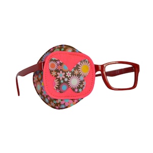 Puede incluir: Una gafa con montura roja con un parche para el ojo floral marrón y rosa con un diseño de mariposa.
