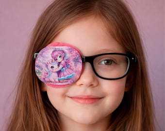 May include: A pink eye patch with a colorful illustration of a girl hugging a unicorn, worn over the left eye. The eye patch is held in place by black framed glasses. The background is a soft pink.