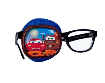 May include: Blue eye patch with a brown border and a Cars themed image of Lightning McQueen and Mater. The eye patch is attached to a pair of black framed glasses.