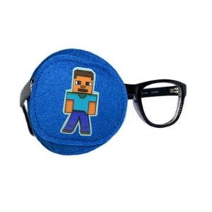 以下が含まれることがあります： Minecraftのキャラクターが描かれた青い眼帯。眼帯は黒いフレームの眼鏡に取り付けられています。