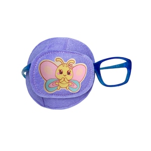 Puede incluir: Parche para el ojo morado con un diseño de mariposa y gafas con montura azul. La mariposa tiene un cuerpo amarillo, alas rosas y una flor en la cabeza.