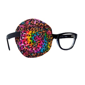May include: A black eye patch with a colorful leopard print design is attached to a pair of black framed glasses. The glasses have clear lenses and the text "Cat 53300" is printed on the right temple.