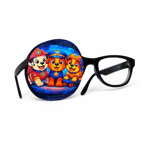 Peut inclure: Lunettes à monture noire avec un cache-œil décoratif. Le cache-œil est rond, de texture denim, et présente une image de dessin animé colorée de trois chiots en uniforme. Les chiots portent des tenues rouges, bleues et jaunes.