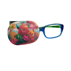 Könnte beinhalten: Ein farbenfroher Augenklappen mit einem Design aus vier Comic-Monstern. Die Klappe ist an einer blauen Brille befestigt.
