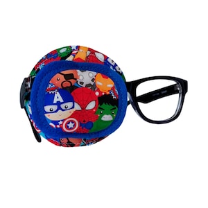 Può includere: Un cerotto per l'occhio blu a tema supereroi con personaggi come Spiderman, Capitan America e Hulk. Il cerotto è attaccato a un paio di occhiali con montatura nera.
