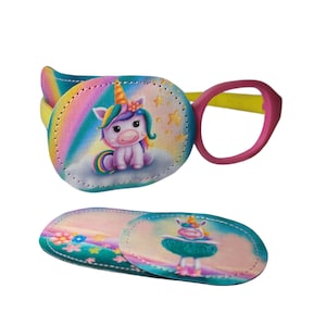 Könnte beinhalten: Ein Set mit zwei Augenklappen mit einem Einhorn-Motiv. Eine Klappe hat einen Regenbogen-Hintergrund mit einem Einhorn, das auf einer Wolke sitzt. Die andere Klappe zeigt ein Einhorn mit einem rosa und blauen Hintergrund. Die Klappen sind aus weichem, bequemem Material gefertigt und eignen sich perfekt zum Abdecken eines Auges.