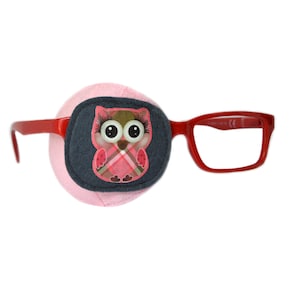 Puede incluir: Un parche para el ojo rosa con un diseño de búho azul y rosa. El parche para el ojo está unido a unas gafas de plástico rojo.