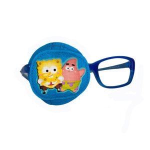 Può includere: Cerotto per l'occhio blu con un design di cartoni animati di SpongeBob SquarePants e Patrick Star. Il cerotto è attaccato a un paio di occhiali con montatura blu.