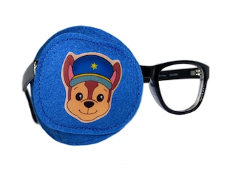 May include: Blue eye patch with a cartoon character wearing a police hat. The character has brown fur, a yellow star on his hat, and a friendly expression. The eye patch is attached to black framed glasses.