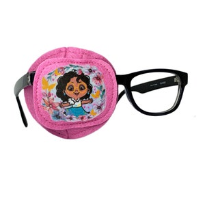 May include: Pink eye patch with a cartoon girl wearing glasses and flowers on it. The eye patch is attached to black framed glasses.