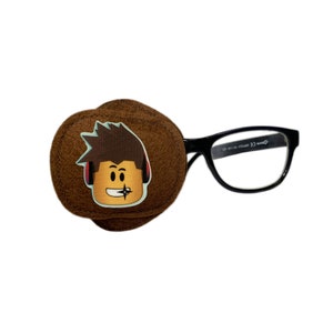 May include: A brown eye patch with a cartoon character wearing headphones printed on it. The eye patch is attached to black framed glasses.
