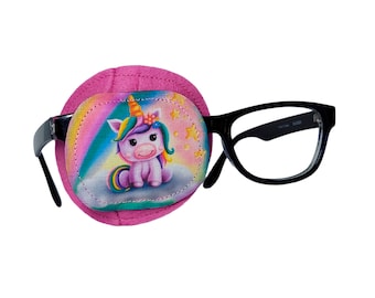 May include: Pink eye patch with a unicorn design. The patch has a rainbow background with stars and a unicorn sitting on a cloud. The patch is attached to a pair of black framed glasses.
