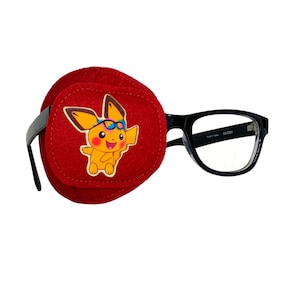 May include: Red felt eye patch with a cartoon character wearing sunglasses. The character is yellow with black markings and is wearing a red headband. The eye patch is attached to black framed glasses.