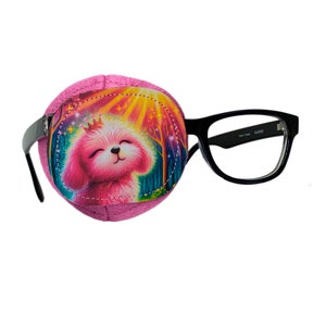 May include: Pink eye patch with a colorful illustration of a dog wearing a crown. The eye patch is attached to a pair of black framed glasses.