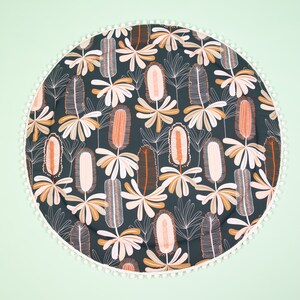May include: A round, dark green play mat with a white pom-pom trim. The mat features a repeating pattern of stylized orange and white flowers.