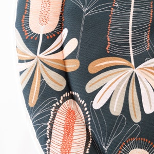 May include: A dark blue fabric with a floral pattern featuring pink, orange, and white flowers. The fabric has a textured surface and a repeating pattern.