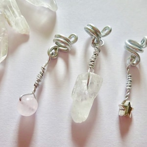 May include: Three silver wire wrapped crystal pendants. The first pendant features a pink crystal, the second a clear crystal, and the third a silver star.