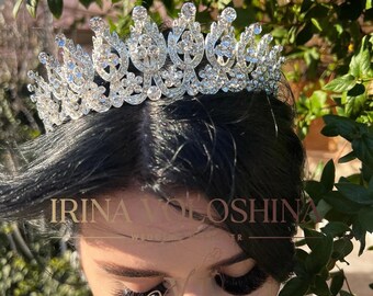May include: A silver-toned tiara with numerous clear crystals. The tiara is set against a backdrop of green foliage. The text "IRINA VOLOSHINA" is visible in the image.