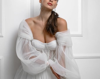 May include: A white wedding dress with a sweetheart neckline and a corset bodice. The dress has large, puffy sleeves and a flowing skirt. The model is wearing the dress and has her hair pulled back in a ponytail. The text "IRINA VOLOSHINA WEDDING DESIGNER" is visible at the bottom of the image.