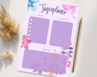 May include: A purple daily planner with watercolor flowers and the text "Tagesplaner" in German. The planner has sections for goals, to-do list, and notes.