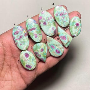 May include: Nine oval and teardrop shaped green and pink gemstones with red and white inclusions. The gemstones are numbered 1 through 9.
