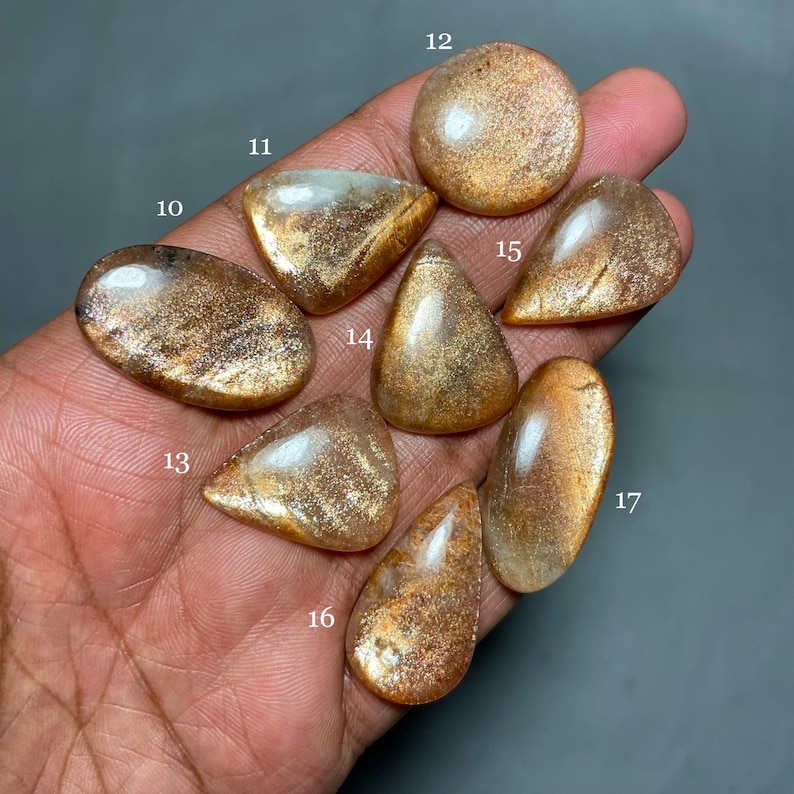 May include: Seven sunstone cabochons in various shapes and sizes, ranging from light gold to dark brown with a shimmery, iridescent finish.