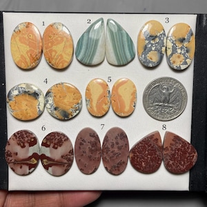 May include: Eight pairs of polished, oval-shaped, natural stone cabochons. The stones are in various colours and patterns, including orange, brown, red, green, and white. The stones are numbered 1 through 8.
