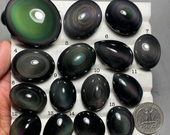 May include: An assortment of polished rainbow obsidian stones in various shapes, including oval and teardrop. The stones display iridescent swirls of green, purple, and black. A US quarter is included for size comparison.