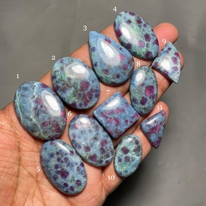 May include: Eleven assorted cabochon gemstones in various shapes and sizes, including oval, teardrop, and square. The gemstones are a mix of blue and green with red flecks.